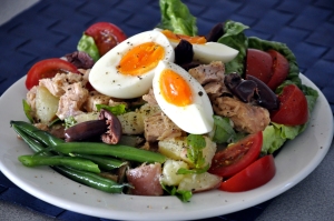a plate of salade nicoise , tuna, ripe red tomatoes, lightly cooked green beans, potato salad, olives  and soft boiled egg